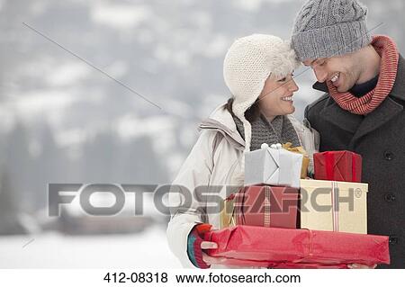 Happy couple carrying Christmas gifts in snow View Large Photo Image Stock Photo - Happy couple carrying Christmas gifts in snow. Fotosearch