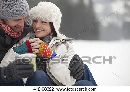 Stock Image - Happy couple drinking coffee in snow. Fotosearch