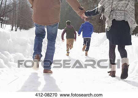 Stock Image - Happy couple holding hands and watching boys run in snowy lane. Fotosearch