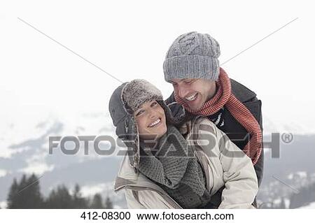 Stock Image - Portrait of enthusiastic couple hugging with mountains in background. Fotosearch