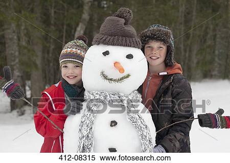 Stock Photography - Portrait of happy boys posing with snowman. Fotosearch