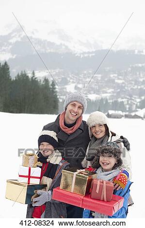 Picture - Portrait of happy family carrying Christmas gifts in snowy field. Fotosearch