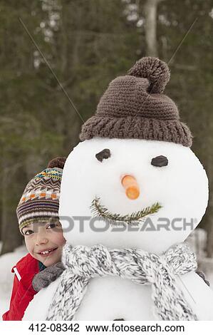 Stock Image - Portrait of smiling boy behind snowman with stocking-cap. Fotosearch