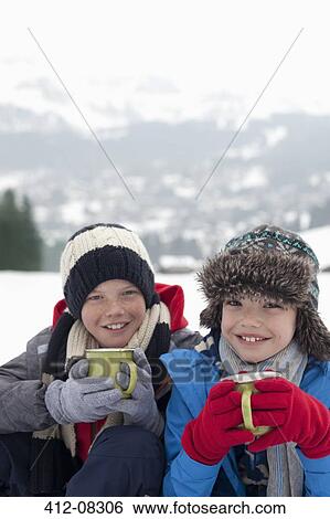 Stock Photograph - Portrait of smiling boys drinking hot chocolate in snowy field. Fotosearch