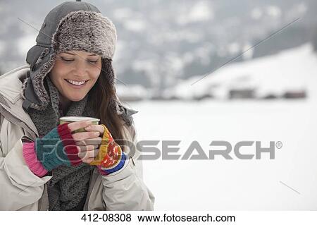 Stock Photo - Smiling woman drinking coffee in snow. Fotosearch