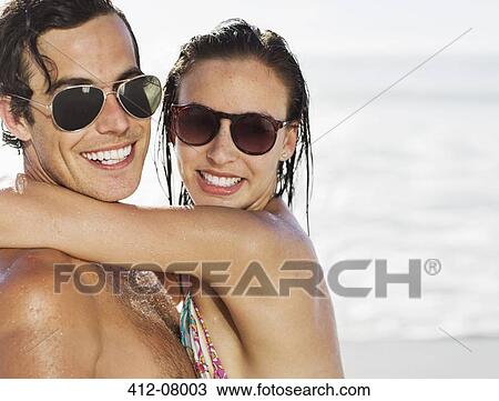 Stock Image - Close up portrait of smiling couple wearing sunglasses on beach. Fotosearch