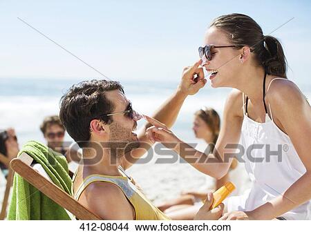 Couple applying sunscreen to each other's nose on beach View Large Photo Image Picture - Couple applying sunscreen to each other's nose on beach. Fotosearch