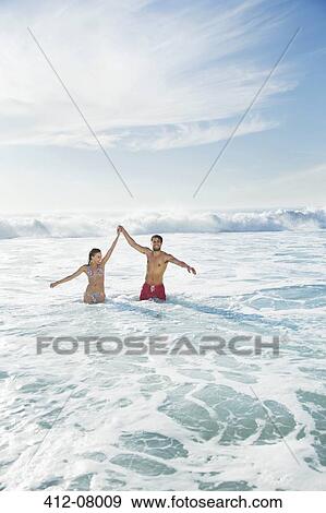 Stock Photo - Couple standing in ocean with arms raised. Fotosearch