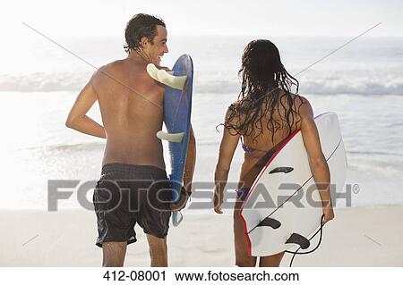 Stock Image - Couple walking with surfboards on beach. Fotosearch