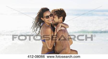 Stock Photograph - Enthusiastic couple hugging on beach. Fotosearch