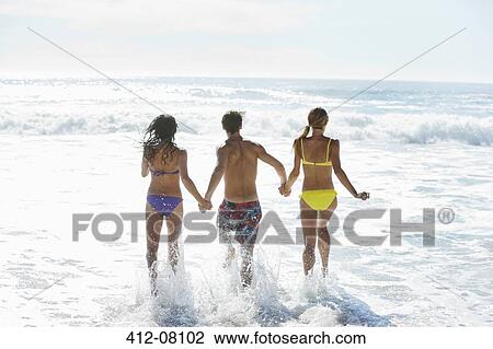 Stock Image - Friends holding hands and running into ocean. Fotosearch