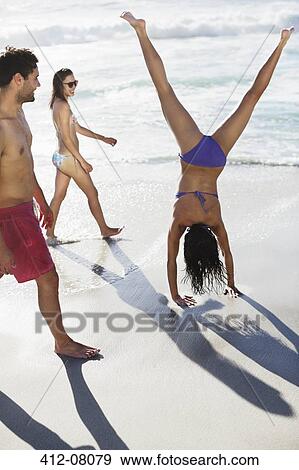 Friends watching woman in bikini doing handstand on beach View Large Photo Image Stock Photo - Friends watching woman in bikini doing handstand on beach. Fotosearch