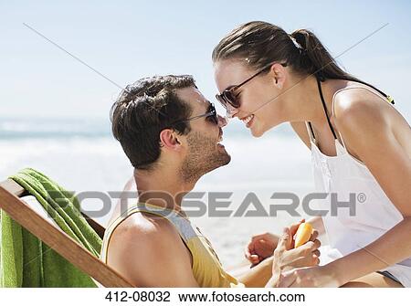 Stock Image - Happy couple rubbing sunscreen-covered noses on beach. Fotosearch