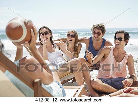 Stock Image - Happy friends with football hanging out at beach. Fotosearch