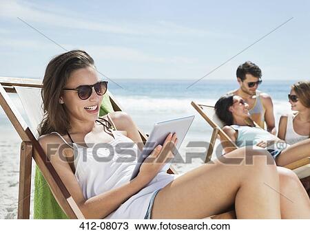 Happy woman using digital tablet in lounge chair on beach View Large Photo Image Stock Image - Happy woman using digital tablet in lounge chair on beach. Fotosearch