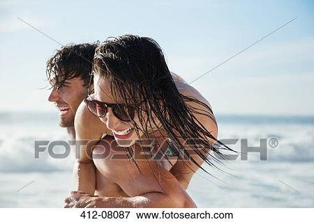 Stock Photo - Man carrying enthusiastic woman on beach. Fotosearch