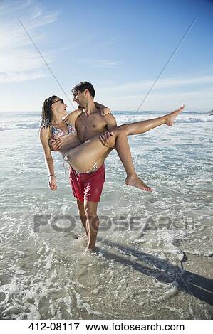 Man carrying woman in ocean surf View Large Photo Image Stock Photo - Man carrying woman in ocean surf. Fotosearch