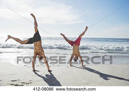 Men in swim trunks doing handstands on beach View Large Photo Image Stock Photograph - Men in swim trunks doing handstands on beach. Fotosearch