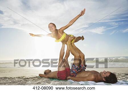 Men lifting woman with legs on beach View Large Photo Image Stock Image - Men lifting woman with legs on beach. Fotosearch
