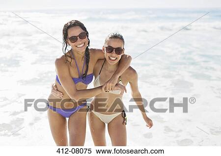Stock Photography - Portrait of enthusiastic friends in bikinis hugging on beach. Fotosearch