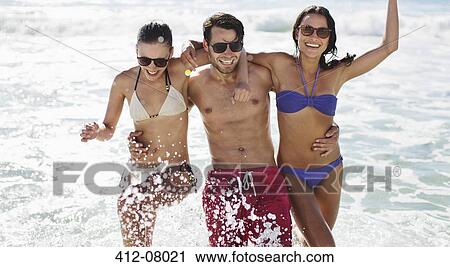 Stock Image - Portrait of enthusiastic friends splashing in ocean. Fotosearch