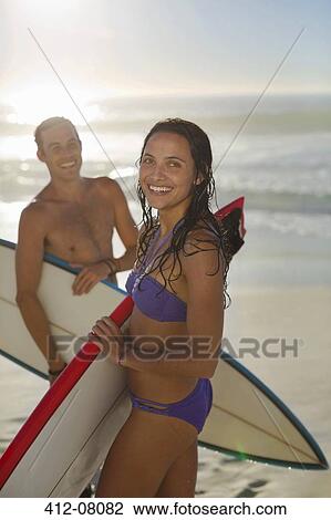 Stock Image - Portrait of happy couple holding surfboards on beach. Fotosearch