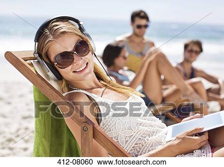 Stock Image - Portrait of happy woman listening to headphones at beach. Fotosearch