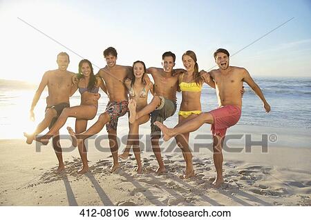 Stock Photograph - Portrait of smiling friends hugging and kicking on beach. Fotosearch