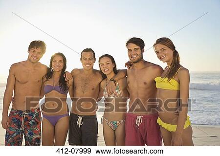 Portrait of smiling friends in bikinis and swim trunks hugging on beach View Large Photo Image Stock Photo - Portrait of smiling friends in bikinis and swim trunks hugging on beach. Fotosearch