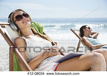 Serene woman listening to headphones in lounge chair on beach View Large Photo Image Picture - Serene woman listening to headphones in lounge chair on beach. Fotosearch