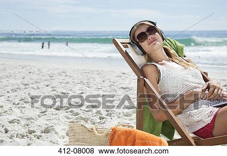 Serene woman listening to headphones in lounge chair on beach View Large Photo Image Stock Photo - Serene woman listening to headphones in lounge chair on beach. Fotosearch