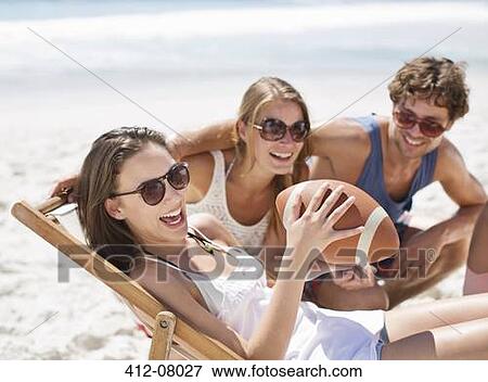 Stock Photo - Smiling friends with football on beach. Fotosearch