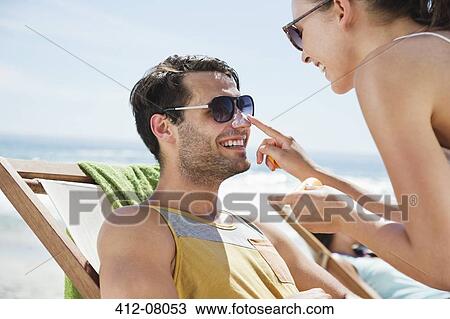 Woman applying sunscreen to man's nose at beach View Large Photo Image Stock Image - Woman applying sunscreen to man's nose at beach. Fotosearch