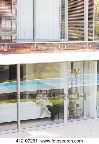 Stock Image - Woman and dog at window of modern house. Fotosearch