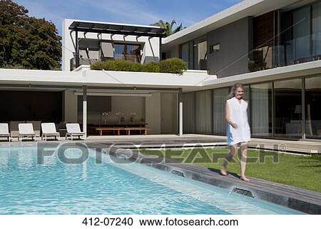 Stock Image - Woman walking along luxury swimming pool. Fotosearch