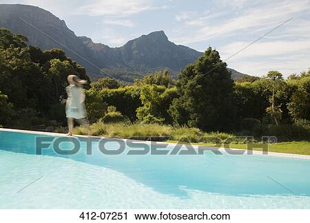 Stock Image - Woman walking along swimming pool. Fotosearch