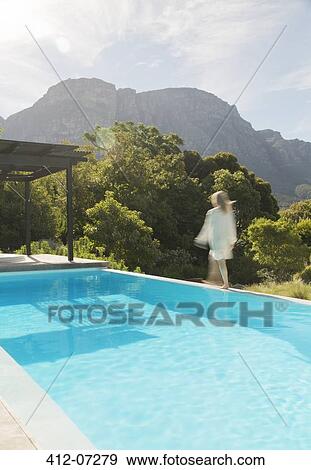 Stock Photo - Woman walking along swimming pool. Fotosearch