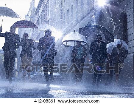 Stock Image - Business people with umbrellas running in rain. Fotosearch