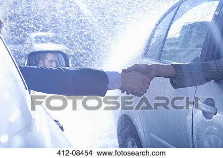 Picture - Businessman and businesswoman extending handshake from cars in rain. Fotosearch