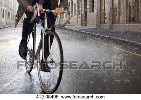 Stock Photograph - Businessman riding bicycle in rainy street. Fotosearch