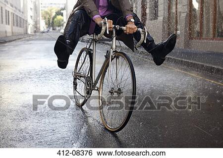 Businessman riding bicycle with feet up in rain View Large Photo Image Stock Photograph - Businessman riding bicycle with feet up in rain. Fotosearch