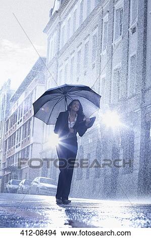 Picture - Businesswoman standing under umbrella in rainy street. Fotosearch