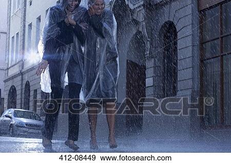 Stock Photo - Businesswomen in ponchos walking in rainy street. Fotosearch