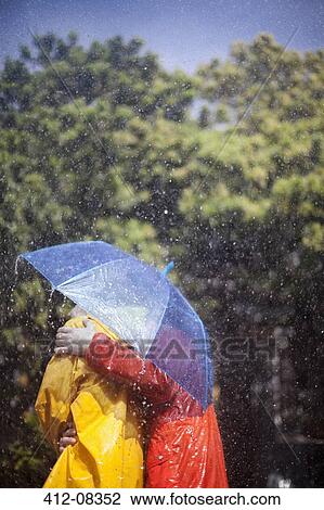 Stock Image - Couple hugging under umbrella in rain. Fotosearch