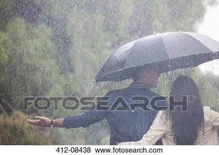Couple walking with arms outstretched under umbrella in rain View Large Photo Image Stock Photo - Couple walking with arms outstretched under umbrella in rain. Fotosearch