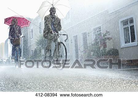 Picture - Couple with umbrellas riding bicycles in rain. Fotosearch