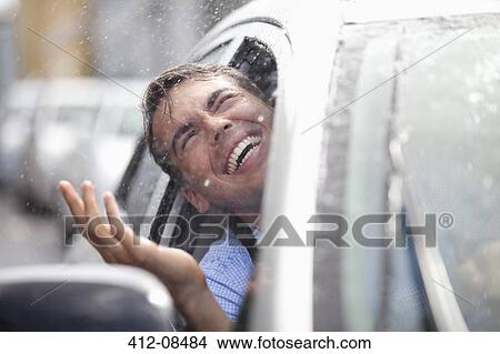 Picture - Enthusiastic man in car looking out window at rain. Fotosearch