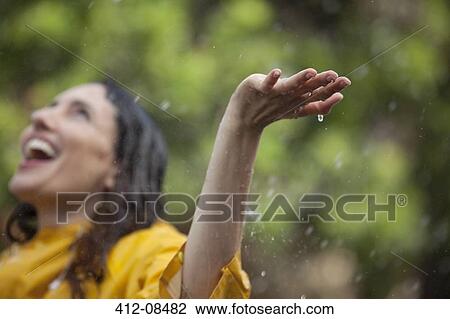 Stock Image - Enthusiastic woman standing with arms outstretched and head back in rain. Fotosearch