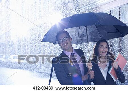 Happy businessman and businesswoman walking under umbrella in rain View Large Photo Image Stock Photo - Happy businessman and businesswoman walking under umbrella in rain. Fotosearch