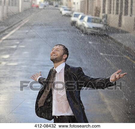 Stock Image - Happy businessman with arms outstretched in rainy street. Fotosearch